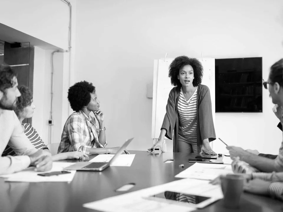 Businesswoman standing and speaking to a group of colleagues seated around a conference table during a meeting.