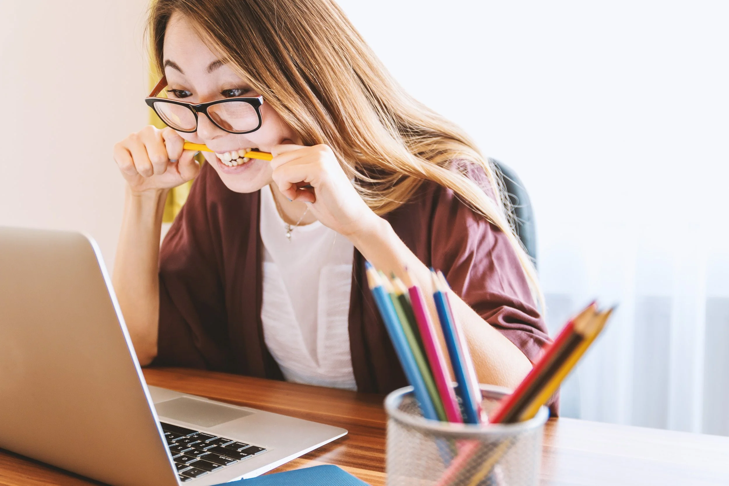 Frustrated woman biting a pencil while looking at her laptop