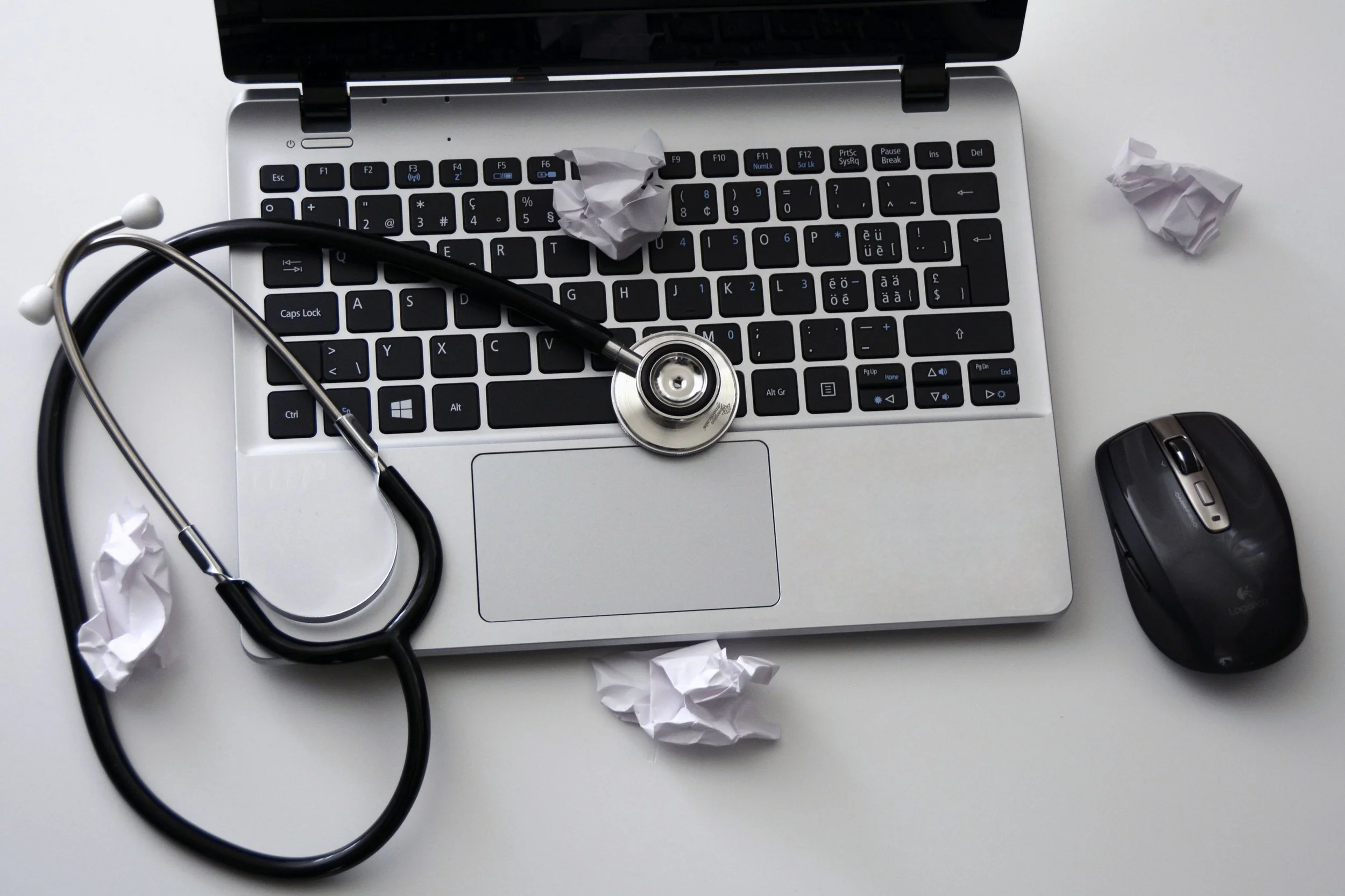 Stethoscope resting on a laptop keyboard surrounded by crumpled paper