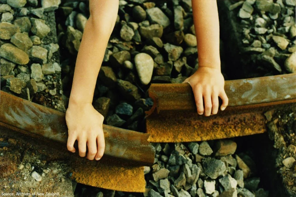 Hands holding two ends of a broken, rusted railway track that do not line up